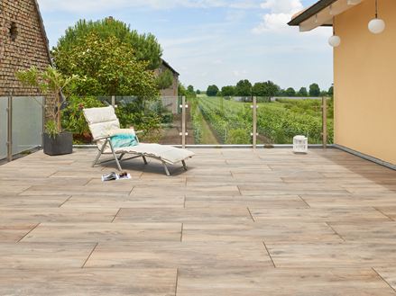 Een ligstoel op een terras met houtlook vloertegels, met een wijngaard op de achtergrond