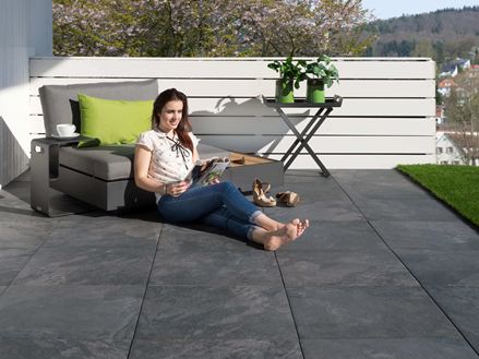 Jonge vrouw leest op terras met donkere porcellanato tegels met leisteenlook en modern meubilair