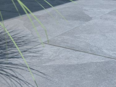 Planten werpen schaduw op terras met platen met alpine grijs leigeffect
