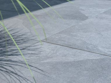 Planten werpen schaduw op terras met platen met alpine grijs leigeffect