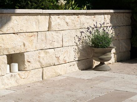 Natuurstenen muur van lichtgekleurd natuursteen met plantendek ervoor en aangrenzende natuurstenen vloer van travertin