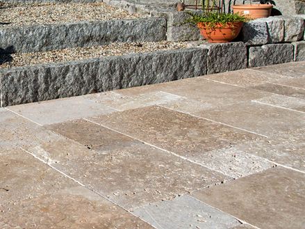 Terras met natuurstenen platen van bruin travertin, op de achtergrond een trap met granieten stenen