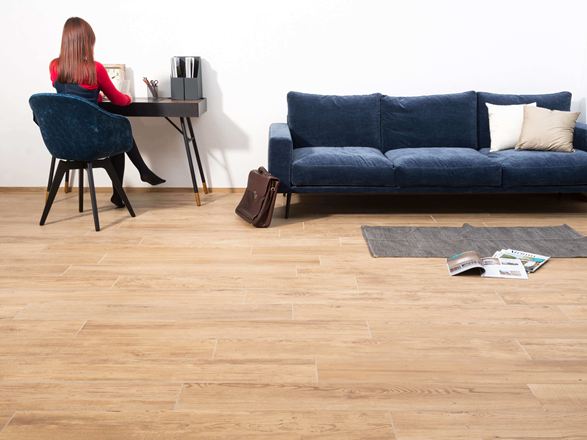 Vrouw zittend aan een tafel naast een bank in een woonkamer met houtlook porcellanato tegels als vloerbedekking