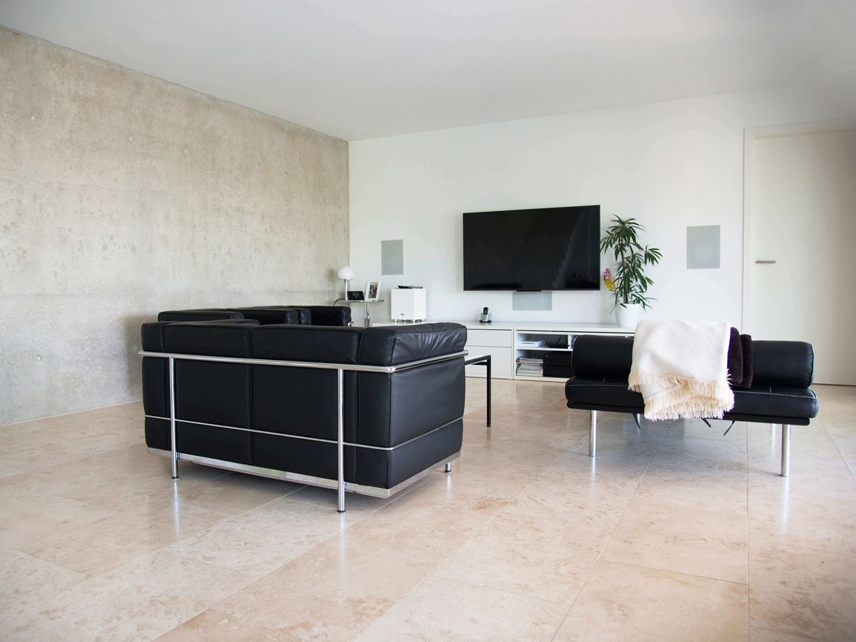 Moderne woonkamer met zwarte banken en lichtbeige Classic Light travertin tegels als vloerbedekking