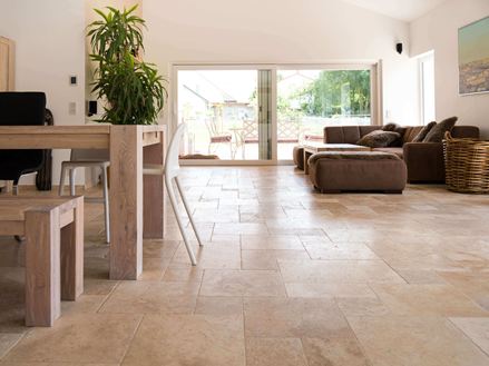 Woonkamer met bruine bank, witte muren en medium travertin tegels in bruin-beige als vloerbedekking