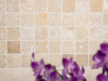 Paarse bloemen tegen een beige-bruin travertinmozaïek