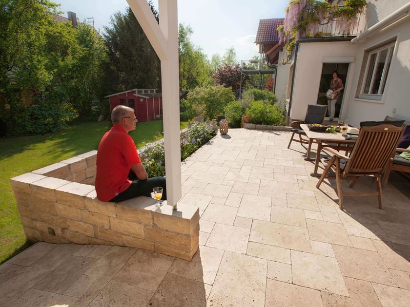 Man zittend op terras met lichtgekleurd travertin in Romeinse band en natuurstenen terras
