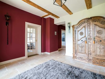 Entree met houten kast, een rode muur en beige travertin tegels