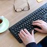 Handen op toetsenbord, bril en een kop koffie ernaast