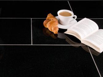 Donkere Nero Assoluto tegels met croissant, koffiekopje en een open boek