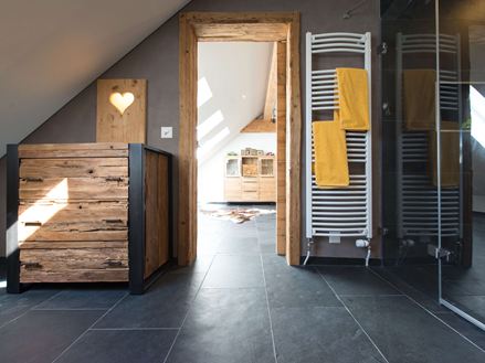 Rustieke badkamer met houten meubels, donkere natuurstenen tegels van leisteen als vloer en een dakhelling
