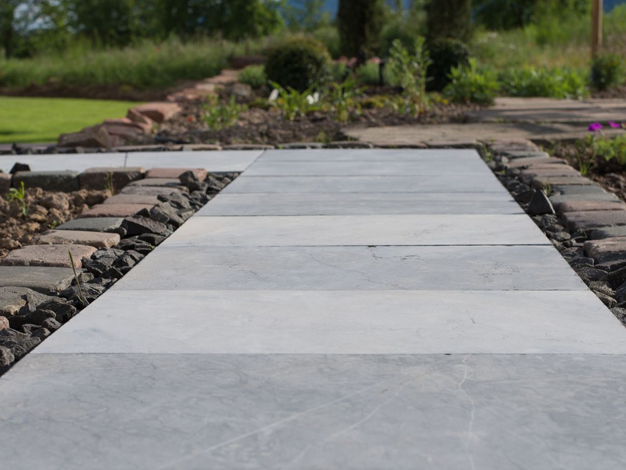 Hardstenen platen als tuinpad, met bloembedden en een groen gazon op de achtergrond