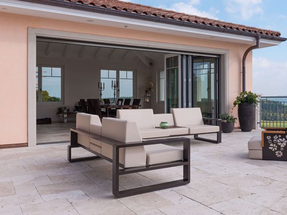 Terras met moderne tuinmeubelen en brede glazen pui naar het interieur op Licht travertin plaat