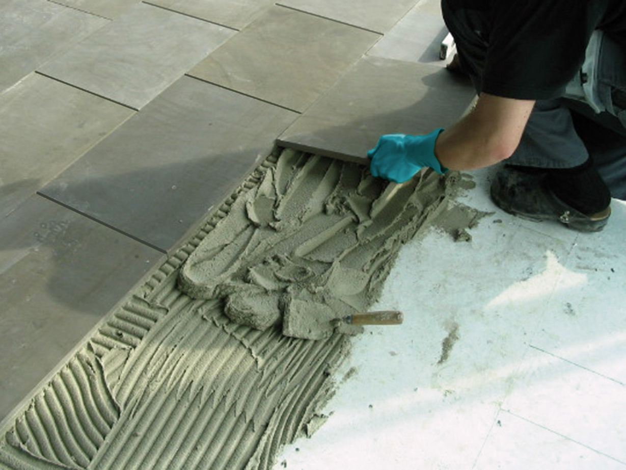 Installateur legt tegels in het dikke bed op een betonnen plaat