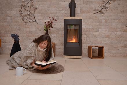 Vrouw liggend op kalkstenen tegels voor een muur met natuurstenen lambrisering en open haard, een boek lezend